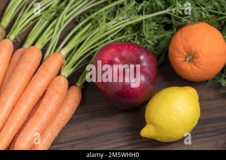 Auswahl an frischen Karotten, Apfel, Orange, Zitrone auf rustikalem Holz. Gesundes Obst und Gemüse mischen sich. Stockfoto
