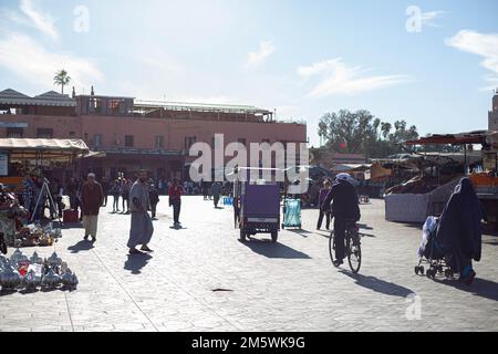 Sonnige Straßenszene in Marrakesch, Marokko. Leute laufen, Wagen, Palmen, Gebäude. Pulsierendes Stadtleben. Stockfoto