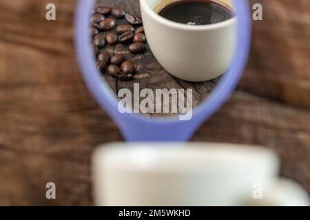 Reflexion einer Tasse Kaffee und Kaffeebohnen in einem kleinen Spiegel. Konzeptuelles Bild der Kaffeepause Stockfoto