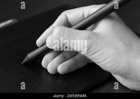 Eine Hand zeichnet mit einem Eingabestift auf einem Grafiktablett. Grafikdesigner und Künstler. Kreative Arbeit, Inspiration und Kunst. Elektronische Kunstgeräte. Schwarz und Stockfoto