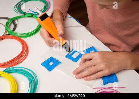 Teenager Girl mit 3D Pen. Drucken mit farbigen Kunststoffdrahtfäden. Kind macht ein Haus, zeichnet mit 3D Stift. Kunst, Robotik. DAMPF, MINT-Pädagogik Stockfoto