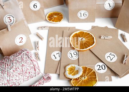 Adventskalender Für Weihnachten. Papiertüten, trockenes Obst, Schnur auf weißem Tisch. Saisonale Aktivität für Kinder, Familienurlaub im Winter. Handgefertigter, gefärbter Kalend Stockfoto