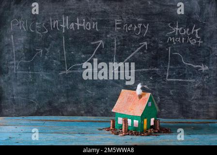 Steigende Mieten, Heizkosten und Preise für Wohnungen, Modellhaus mit gestapeltem Geld vor der Tafel mit Finanzdiagrammen. Kostenloser Kopierplatz Stockfoto