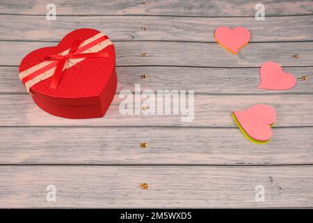 Herzförmiges Geschenk und drei rosa Herzen auf einem Holztisch. Stockfoto