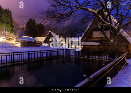 Kleiner Teich vor dem schneebedeckten traditionellen Dorf bei Sonnenaufgang Stockfoto