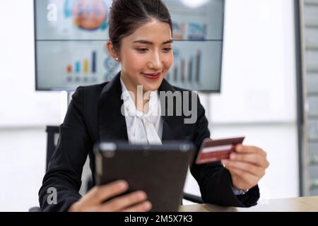 Eine junge Geschäftsfrau, die im Büro arbeitet, verwendet ein Tablet, um die Finanzen zu prüfen, Kreditkarten online zu kaufen Stockfoto