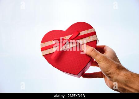 Männerhand, die ein Geschenk in Form eines Herzens auf weißem Hintergrund macht. Valentinstag. Stockfoto