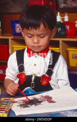 Junger asiatischer Junge, Kindergarten, der im Klassenzimmer sitzt und Aquarelle benutzt Stockfoto