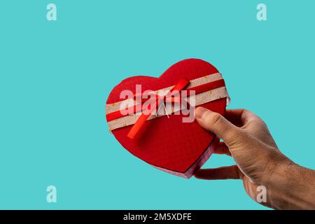 Männerhand, die ein Geschenk in Form eines Herzens auf blauem Hintergrund macht. Valentinstag. Stockfoto