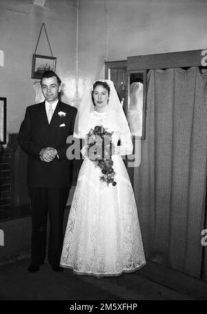 1950, historisch, ein gerade verheiratetes Paar, das in einem Kirchenkostüm für ein Foto steht, England, Großbritannien. Stockfoto