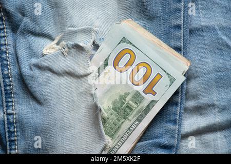 Amerikanische hundert Dollar, die aus einem Loch in Jeans-Nahaufnahme ragen Stockfoto