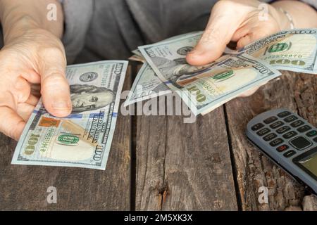 Hände einer alten Frau auf amerikanischen Dollars auf einem Holztisch aus der Nähe Stockfoto