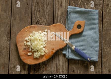 Gehackte Zwiebeln liegen auf einem Holzbrett auf einem Tisch Stockfoto