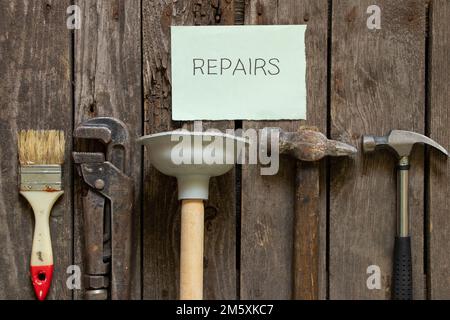 Gasschraubenschlüssel Hammerkolben und Bürste liegen auf einem Holztisch in der Küche und das Wort auf Papier in englischer Reparatur, Reparatur Stockfoto