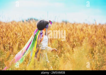 Glückliches kleines Mädchen in einem ukrainischen Kranz spaziert an einem sonnigen Sommertag auf einem Weizenfeld Stockfoto