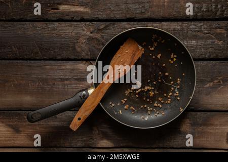 Schmutzige Bratpfanne nach dem Essen auf einem alten Holztisch in der Küche zu Hause, schmutzige Küchenutensilien nach dem Abendessen Stockfoto