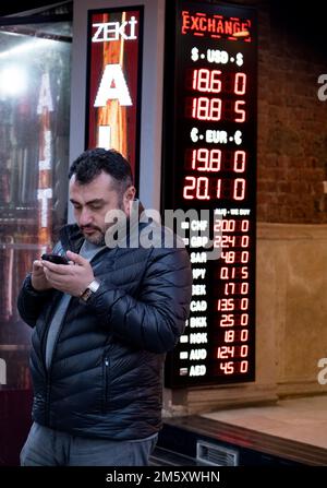 Ein Mann, der auf seinem Handy vor einem Wechselbüro im Eminonu-Bezirk nach Preisen sucht. Istanbul, Eminonu, Türkei - 01. Dezember 2023. Stockfoto