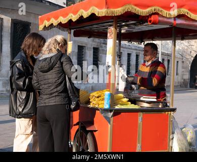 Frauen kaufen bei Händlern. Ein Händler, der Mais auf dem Eminonu-Platz verkauft. Istanbul - Türkei - 31. Dezember 2022. Stockfoto