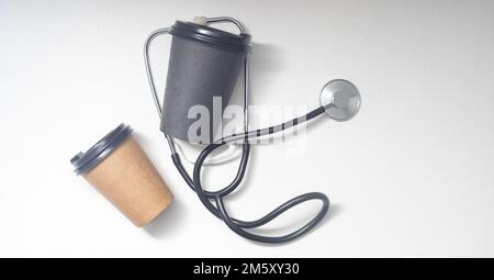 Stethoskop und Kaffee zum Mitnehmen auf weißem Hintergrund. Stockfoto