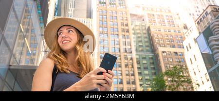 Attraktive positive Frau, die ein Handy in der Hand hält und auf eine moderne Stadt schaut Stockfoto