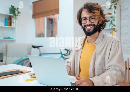 Erfolgreicher hispanischer Freiberufler am Arbeitsplatz, schaut direkt in die Kamera. Stockfoto