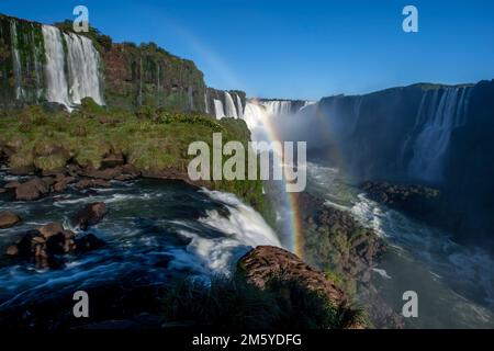 Ein Blick auf die Iguazu-Fälle von der brasilianischen Seite aus mit Blick auf Devil's Throat in der Ferne. Im Canyon ist ein Regenbogen zu sehen. Stockfoto