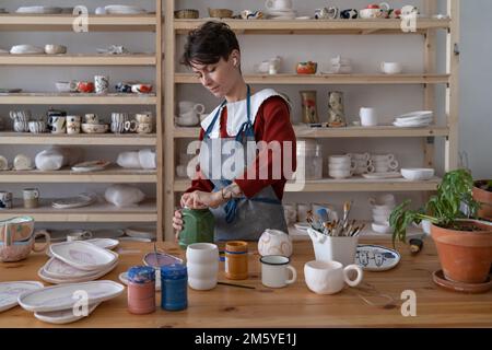 Junge Frau verbringt Zeit im Keramikstudio und arbeitet entspannt und glücklich an Töpferwaren Stockfoto