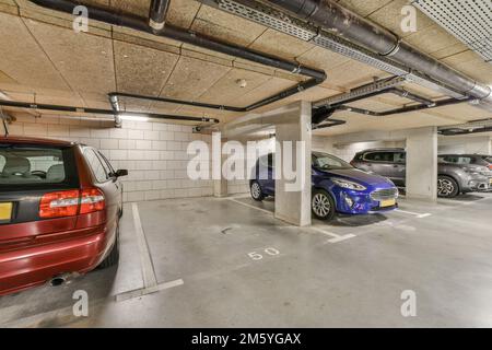 Eine Tiefgarage mit Autos, die auf dem Parkplatz geparkt sind, und zwei Personen, die auf beiden Seiten der anderen Fahrzeuge stehen Stockfoto