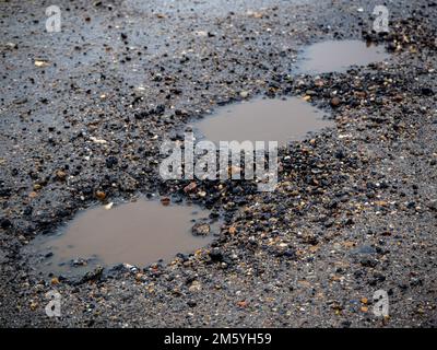 Schlagloch auf einer gepflasterten Straße an einem regnerischen Wintertag. Risikobegriff und Verkehrsprobleme Stockfoto