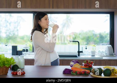 Charmante asiatische Schwangere, die Milch aus Glas trinkt. Attraktive Frau braucht Protein und Kalzium für ihr Baby und es macht sie gesund und stark. Stockfoto