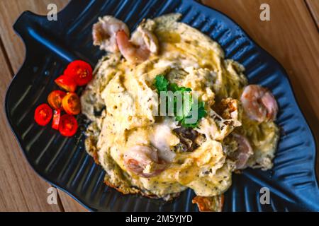 Thailändisches Essen mit Rührei mit Garnelen über Reis auf einem wunderschönen schwarzen Blattteller, Dekoration eines kleinen Korianderblattes, Bild von oben Essen auf einem Stockfoto