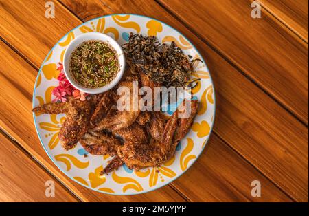 Frittierte Hähnchenflügel mit Kräutern, traditionelles thailändisches Essen, frittierte Hähnchenflügel mit scharfer Sauce auf einem Holztisch, Bilderessen von oben. Stockfoto