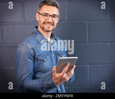 Was würden wir ohne Technologie tun? Porträt eines Mannes, der ein digitales Tablet vor einem Backsteinhintergrund benutzt. Stockfoto