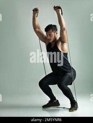 Er steigert seine Fitness-Routine. Studioaufnahme eines jungen Mannes, der mit einem Widerstandsband trainiert, vor grauem Hintergrund. Stockfoto