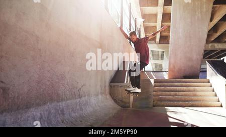 Seine Art Spielplatz. Ein junger Mann, der auf seinem Skateboard im Skatepark Tricks macht. Stockfoto