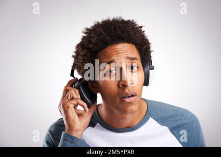 Sag was. Studioaufnahme eines jungen Mannes, der Musik auf seinen Kopfhörern vor grauem Hintergrund hört. Stockfoto