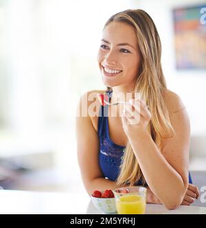 Ich wünsche Ihnen einen fruchtbaren Tag. Eine junge Frau, die zu Hause eine Schüssel Erdbeeren isst. Stockfoto
