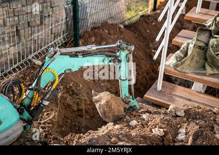 Minibagger gräbt einen Graben, um Rohre zu verlegen. Nahaufnahme eines Baggers, der einen tiefen Graben gräbt. Ein Bagger gräbt einen Graben auf dem Land, um einen zu legen Stockfoto