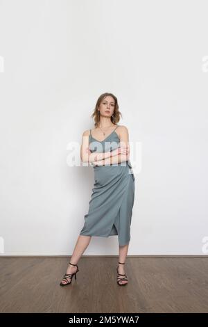 Weibliches Model mit blaugrauem Trägeroberteil aus Seide und gewickeltem Midi-Rock. Stylisches einfarbiges Sommeroutfit. Modestudio-Aufnahme. Stockfoto