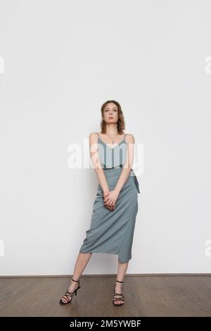 Weibliches Model mit blaugrauem Trägeroberteil aus Seide und gewickeltem Midi-Rock. Stylisches einfarbiges Sommeroutfit. Modestudio-Aufnahme. Stockfoto