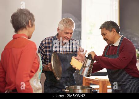 Das wird Ihnen den Moment geben, in dem Sie schmelzen. Eine Gruppe von Senioren, die in der Küche kochen. Stockfoto
