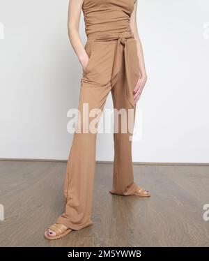 Studiofoto einer Frau in beigefarbenem Baumwolloutfit, Hemd mit Ärmeln und einfacher Hose. Stockfoto