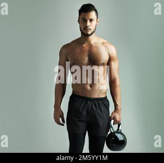 In Topform bleiben. Studioaufnahme eines jungen Mannes, der mit einer Wasserkessel-Glocke trainiert, vor grauem Hintergrund. Stockfoto