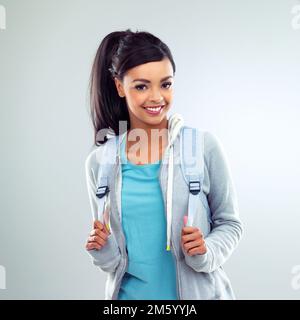 Hören Sie nie auf zu lernen, denn das Leben hört nie auf zu lehren. Ein hübscher junger Schüler, der einen Rucksack auf grauem Hintergrund trägt. Stockfoto