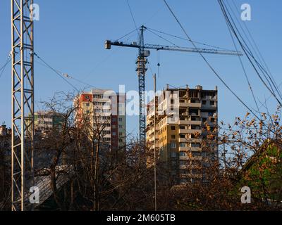 Ein Blick auf ein Gebäude, das im Bau ist und in dessen Nähe ein Kran am blauen Himmel steht. Im Vordergrund befindet sich ein hoher Metallturm mit Halteseilen Stockfoto