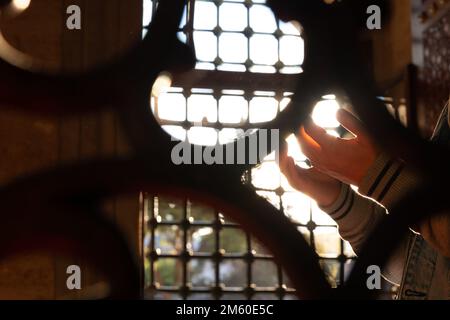 Islamisches Foto. Muslimischer Mann betet in der Moschee hinter den Zäunen. Selektive Fokussierung auf die Hände. Ramadan oder kandil oder Laylat al-qadr oder islamisches Konzert Stockfoto