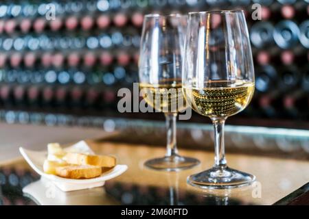 Weinprobe im Weingut, 2 Gläser Weißwein mit Toast und Käse mit Hunderten von Weinflaschen im Hintergrund, Lanzarote, Spanien Stockfoto