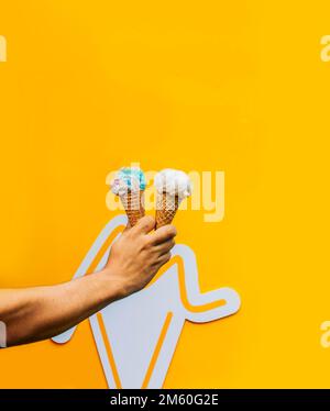 Eine Hand, die zwei Waffeleis isoliert hält. Hand hält zwei Eiskegel auf gelbem Hintergrund. Waffelkonus-Eiscreme-Konzept auf Gelb Stockfoto