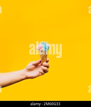 Handgehaltene Eiskrem auf gelbem Hintergrund. Eine Hand, die ein Waffeleis in der Hand hält. Waffelkonus-Eiscreme-Konzept auf gelbem Hintergrund Stockfoto