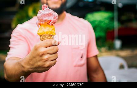 Vorderansicht der Hände einer Person, die einen Eiskegel hält. Unbekannte Leute, die draußen Eiscreme in Zapfen halten. Leute, die ein doppeltes Eis zeigen Stockfoto